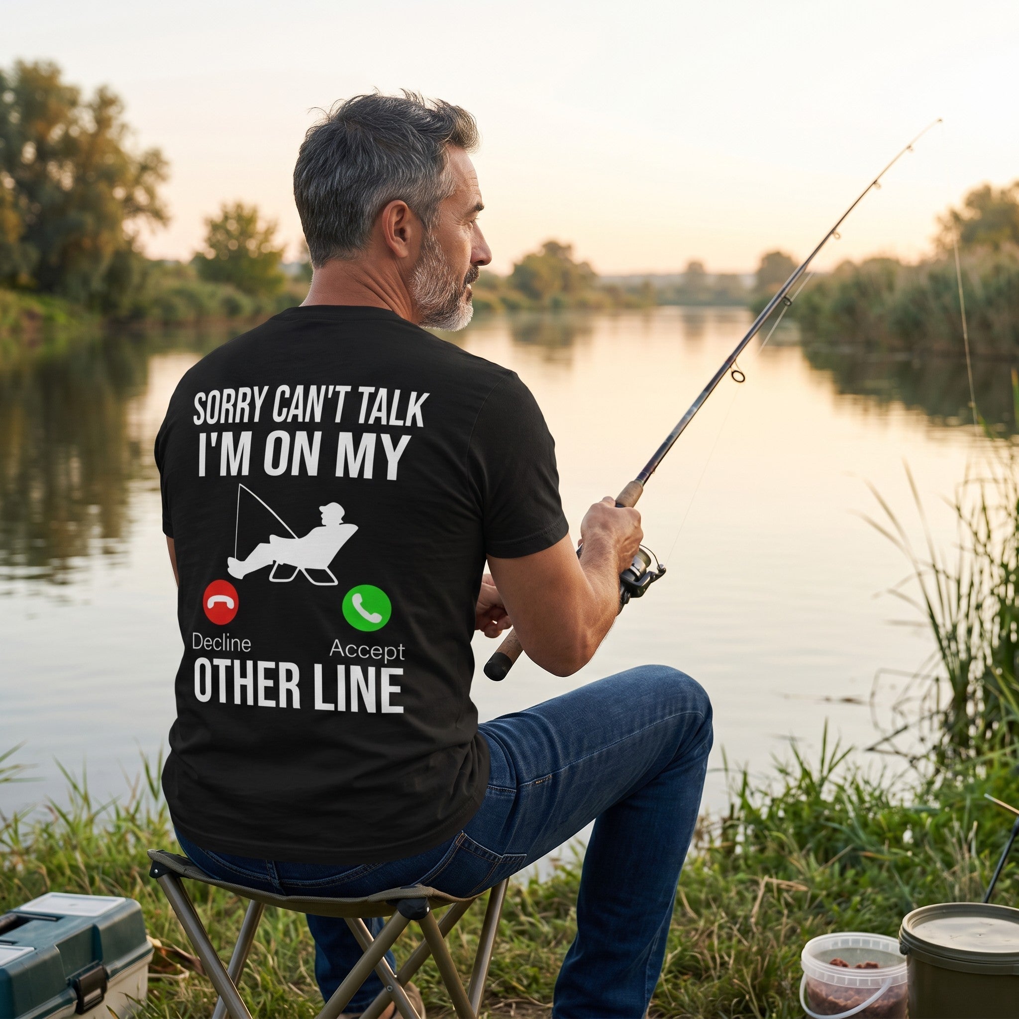 TrendyShift.Com black cotton t-shirt with Sorry Can't Talk I'm On My Other Line fishing graphic worn by a man fishing